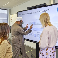  Three people are working together on a large interactive screen in the Cloud Resilience Lab.