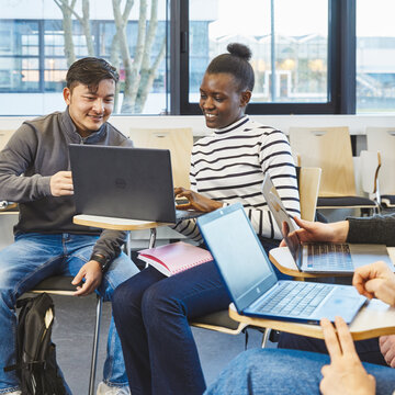 Studierende am Laptop im Austausch - Vorbereitung auf globale Managementaufgaben Studierende sitzen in einer Lerngruppe in einem hellen Raum mit großen Fenstern. Im Fokus sind drei Personen, die gut gelaunt an ihren Laptops arbeiten und sich austauschen.