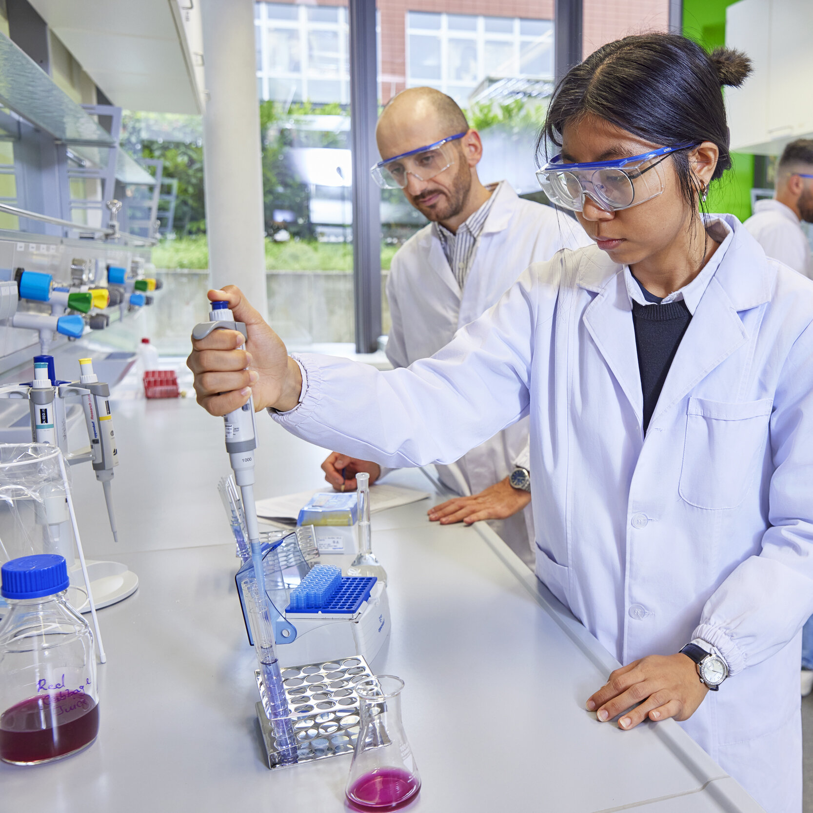 Studierende mit Schutzbrille arbeiten in einem Labor mit einer Pipette und Reagenzgläsern.