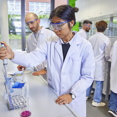 Studierende mit Schutzbrille arbeiten in einem Labor mit einer Pipette und Reagenzgläsern.