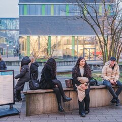 Late one afternoon in January, several students are sitting on the seating areas on the Kamp-Lintfort campus. They are laughing and chatting. The surrounding windows are bathed in a golden-yellow light.