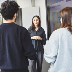 A woman is standing in front of a presentation showing the possible progression of a degree course. A man and a woman are listening.