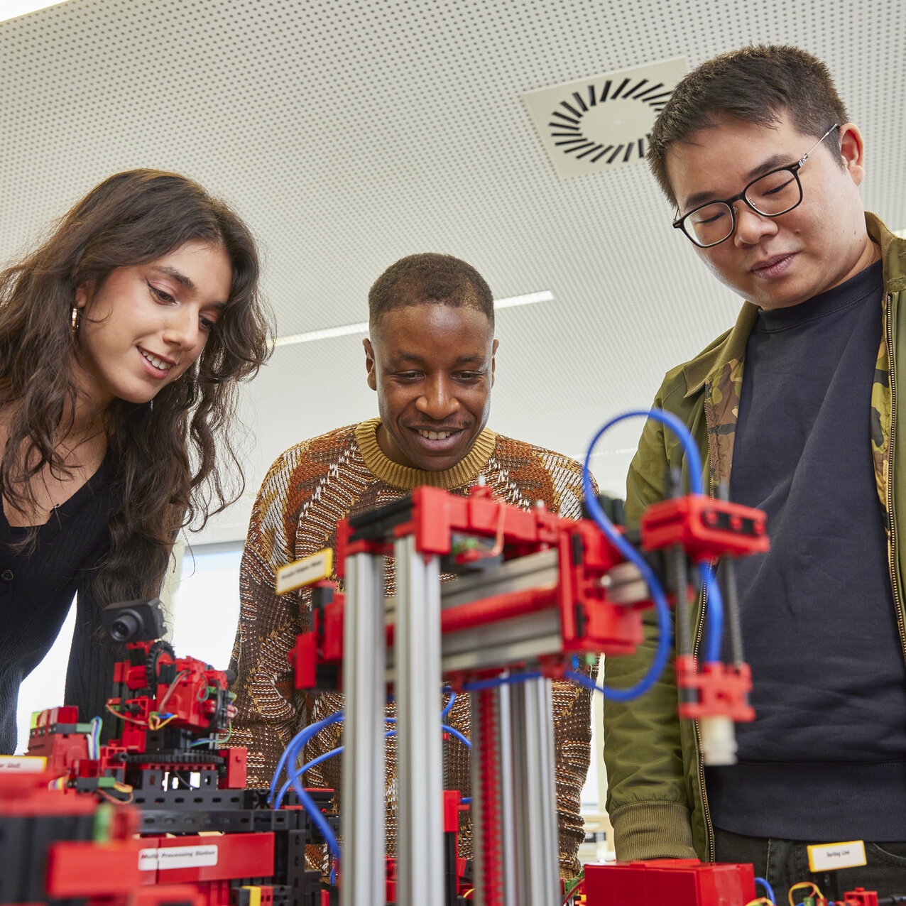 Vier Studierende betrachten gemeinsam die technischen Komponenten einer Modellfabrik.