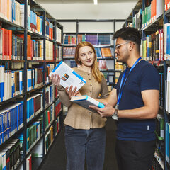 Ein Bibliotheksmitarbeiter zeigt einer Studentin in der Bibliothek Kamp-Lintfort Bücher am Bücherregal
