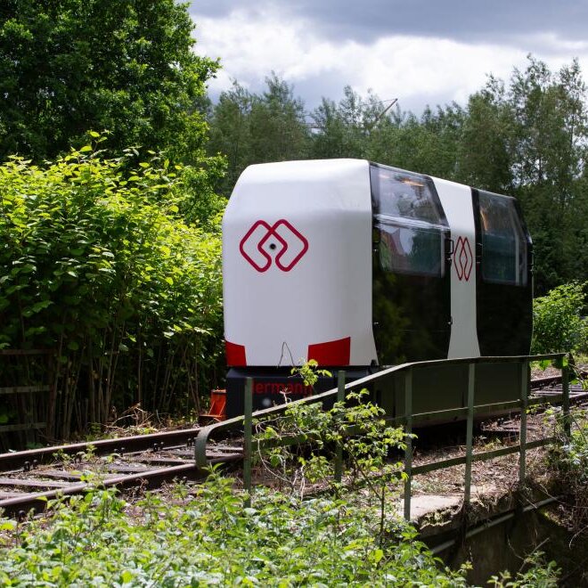 Ein Monocab-Wagon fährt auf einer Bahnschiene durch eine Landschaft
