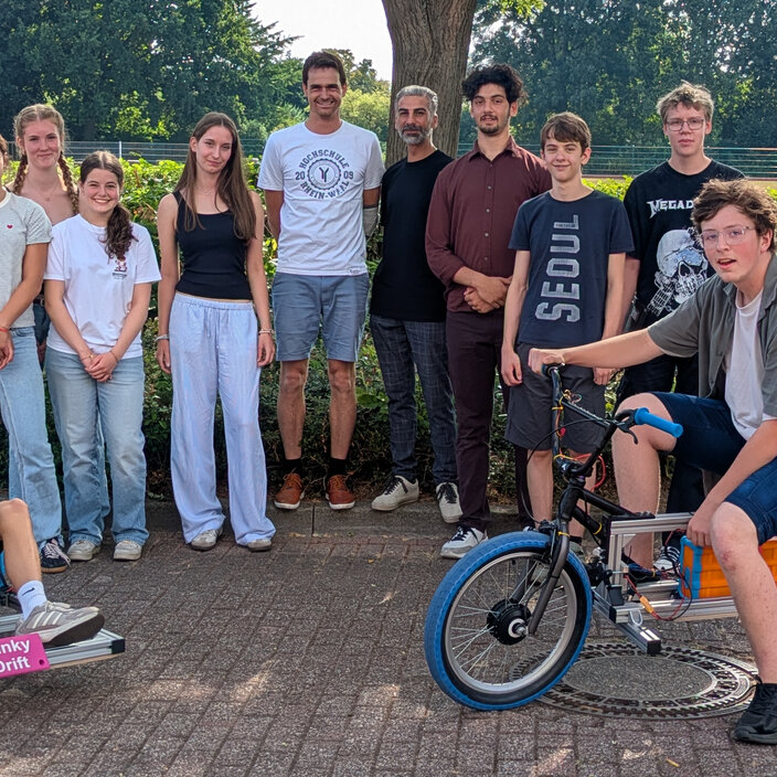 Schülerinnen und Schüler posieren mit ihren selbstgebauten Elektrofahrzeugen, einem Gokart und einem Motorrad.