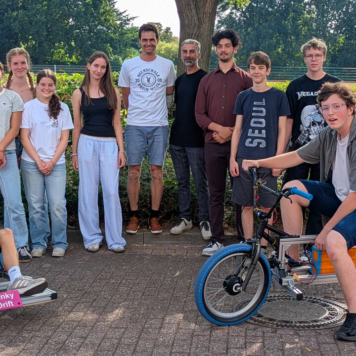 Schülerinnen und Schüler posieren mit ihren selbstgebauten Elektrofahrzeugen, einem Gokart und einem Motorrad.