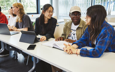 International & Englischsprachig Mehrere Studierende unterschiedlicher Ethnien sitzen in einem Seminarraum an einem Tisch ins Gespräch vertieft