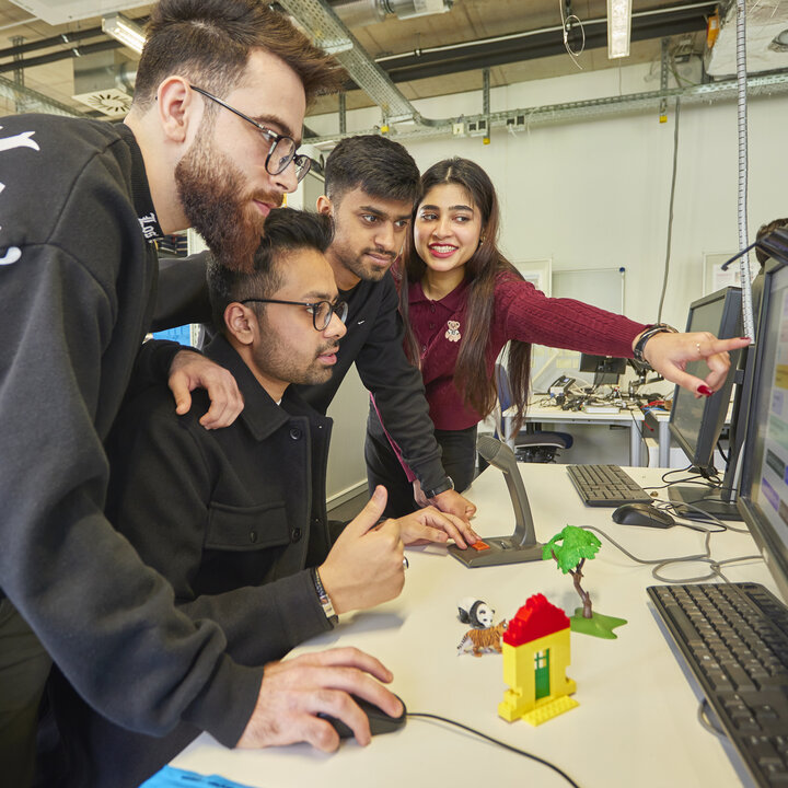 Vier Studierende schauen im AIS-Lab auf einen Computerbildschirm, eine zeigt darauf.