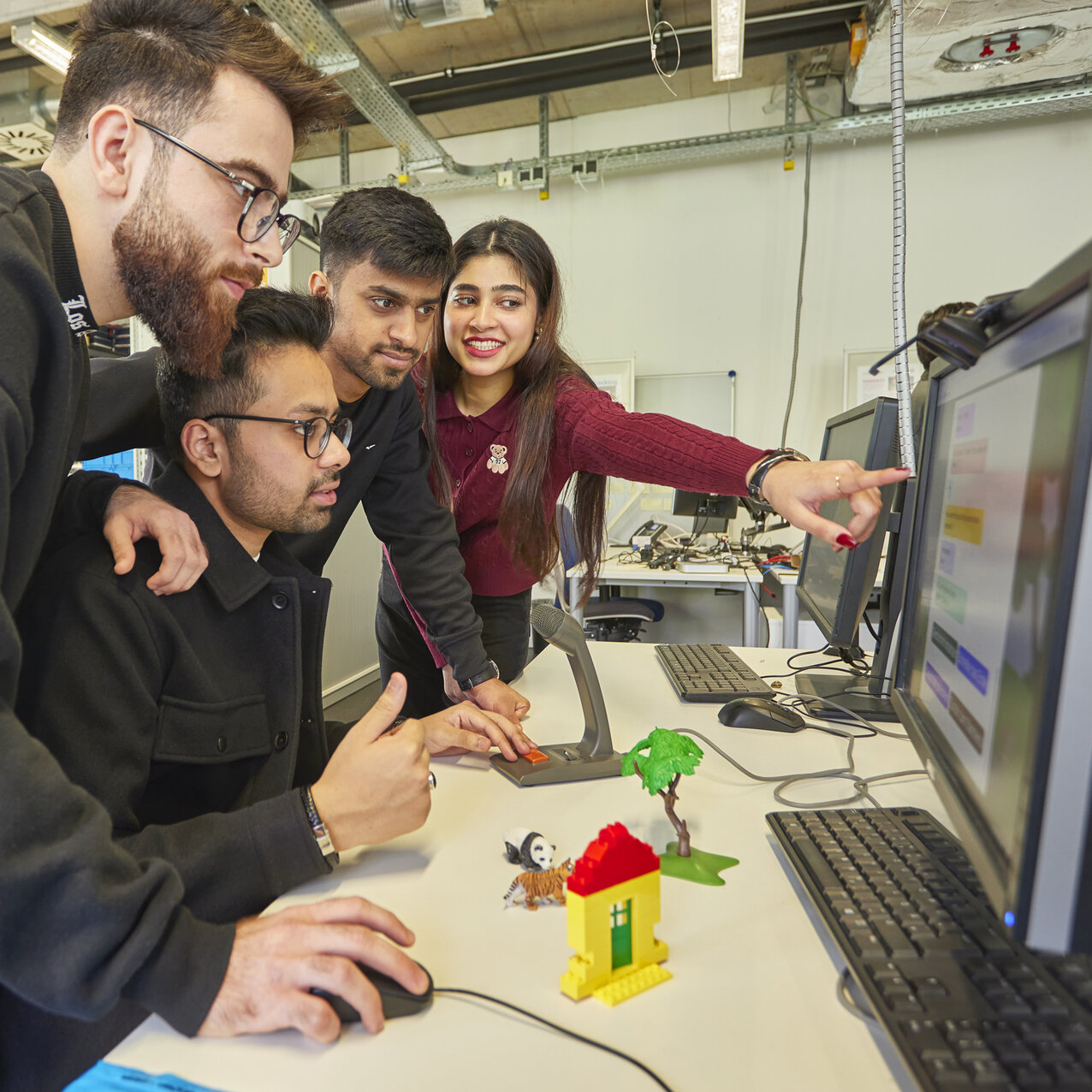 Vier Studierende schauen im AIS-Lab auf einen Computerbildschirm, eine zeigt darauf.