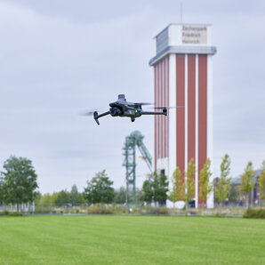 Drohne fliegt über einer Grünfläche, im Hintergrund steht der alte RAG-Turm