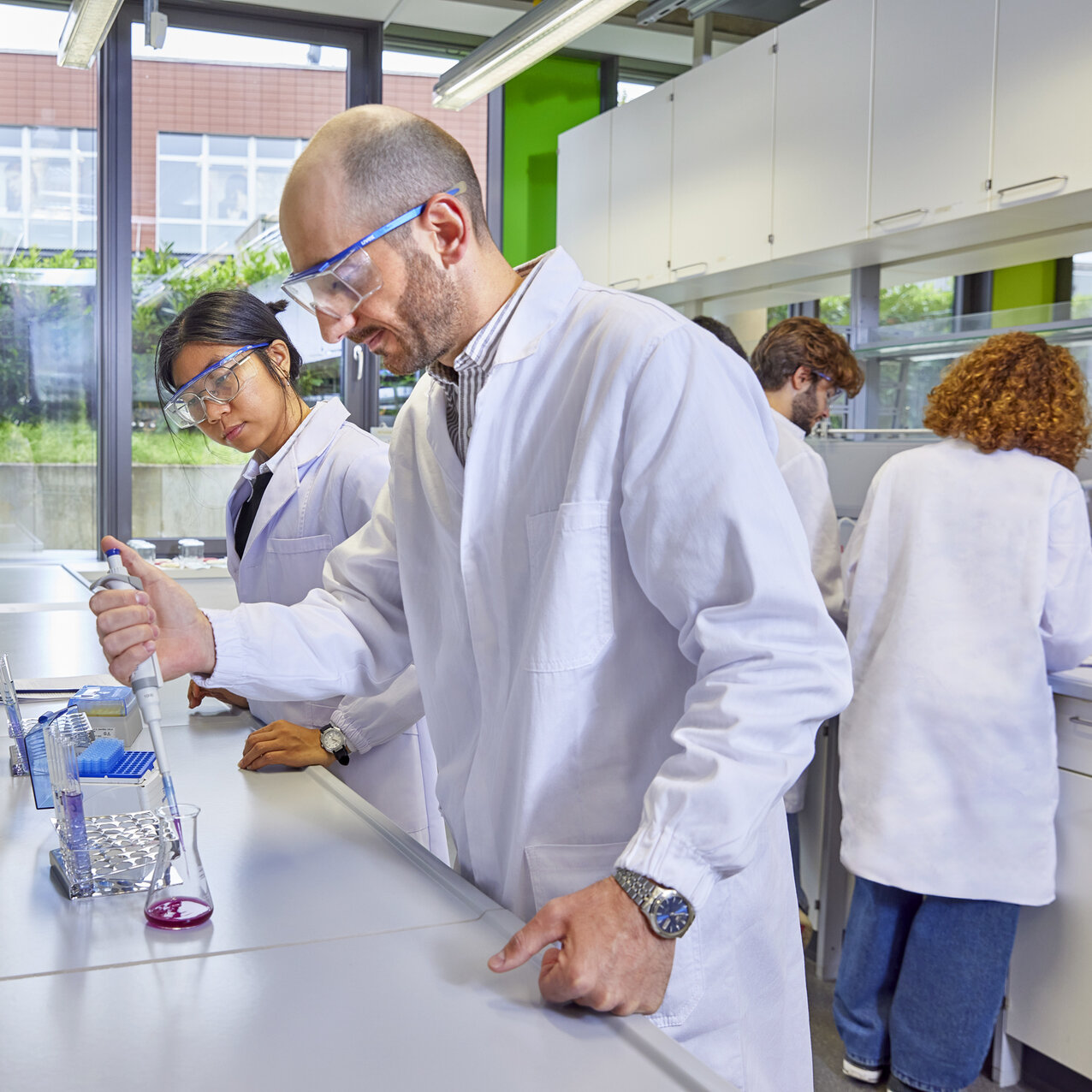 Studierende mit Schutzbrille arbeiten in einem Labor mit einer Pipette und Reagenzgläsern.