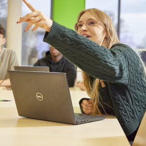 Studentin zeigt vom Laptop aus eine Präsentation und deutet auf etwas