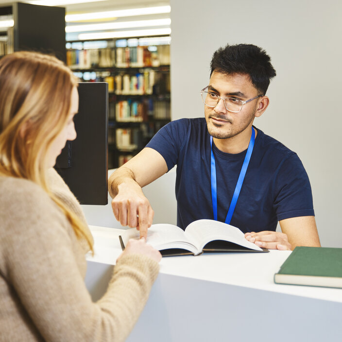 A library member of staff is showing a student something in a book at the information desk in the Kamp-Lintfort library