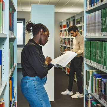 Zwei Studierende schauen sich zwischen Bücherregalen der Bibliothek Kleve Bücher an