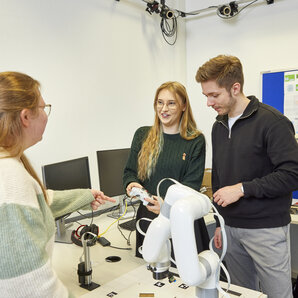 Drei Studierende arbeiten an Projekt mit Roboterarm