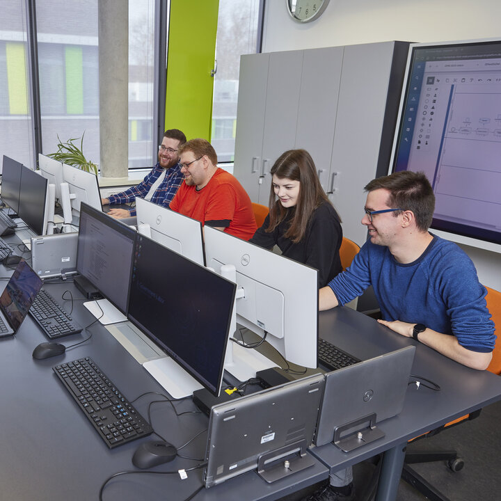 Eine Gruppe von Studierenden sitzt an Computerarbeitsplätzen und blickt auf Bildschirme.