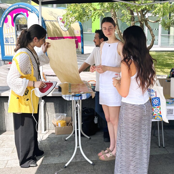 Drei junge Frauen stehen an einem Infostand der Fair Trade University.