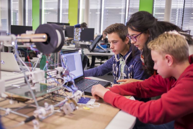 Drei Studierende sitzen am Werktisch und blicken auf den Bildschirm eines Laptops. Sie arbeiten gemeinsam an einem Projekt im FabLab.