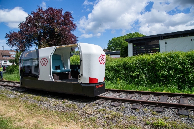 Das autonom fahrende Schienenfahrzeug „MONOCAB” fährt auf einer Bahnschiene an Wohnhäusern vorbei.