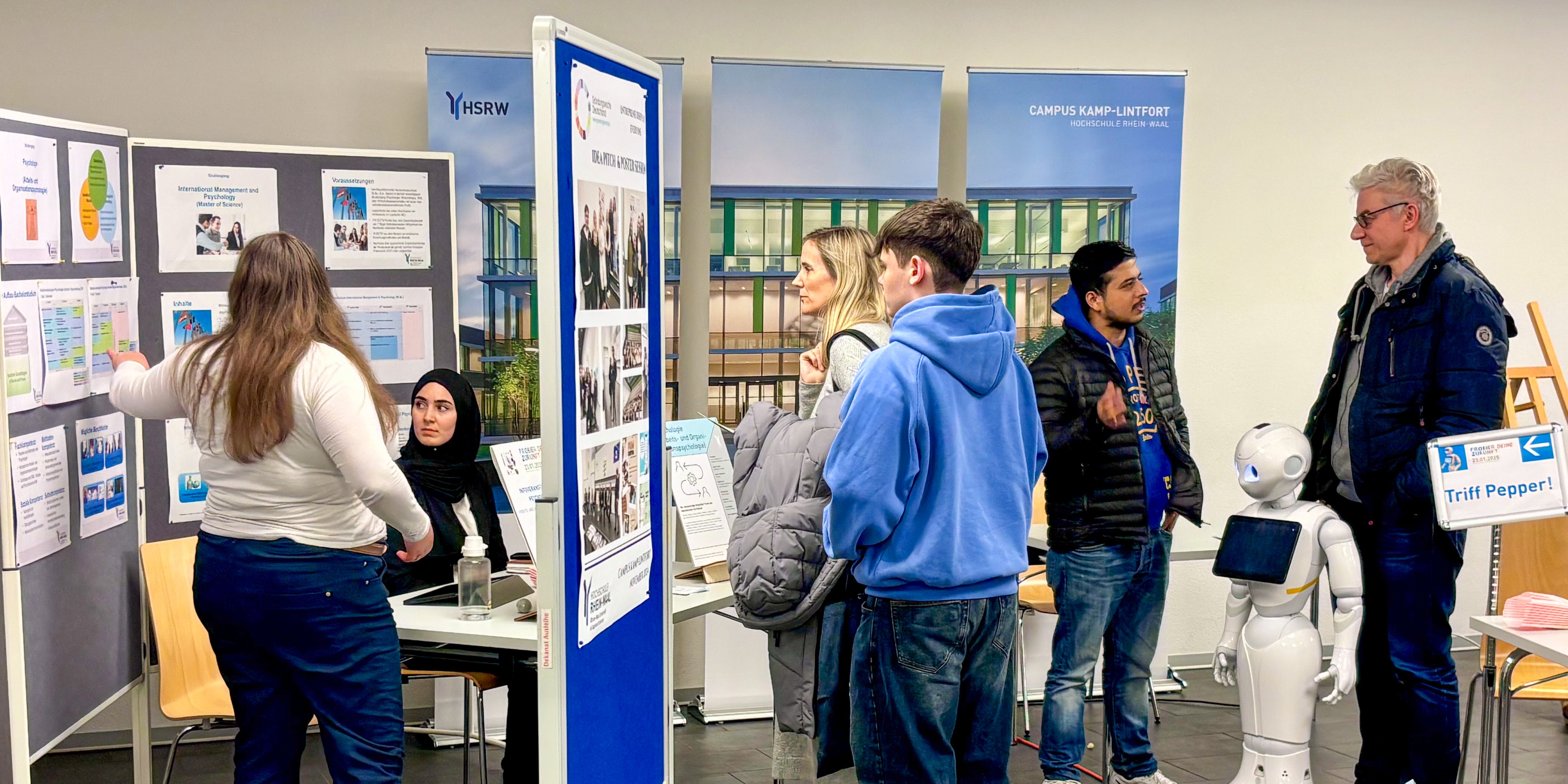 Schülerinnen und Schüler schauen sich Infos zu Studiengängen an Stellwänden und lassen sich von Professoren beraten.