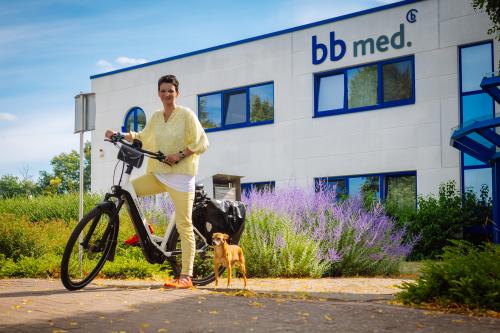 Das Foto zeigt unsere Absolventin Frau Vollmer auf ihrem Fahrrad mit Hund vor dem Firmengebäude von bb med. 