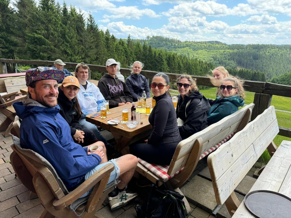 Gruppen Studierender sitzen in der Natur um einen Tisch umnd machen Rast.