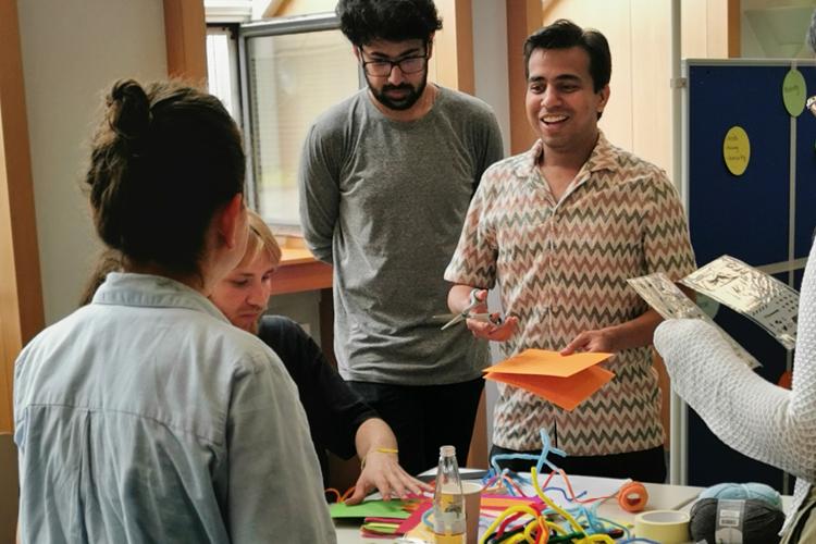 Teilnehmende der StartGlocal Summerschool beim gemeinsamen Brainstorming Teilnehmende der StartGlocal Summerschool beim gemeinsamen Brainstorming. Fünf Personen stehen um einen Tisch mit buntem Papier und unterhalten sich angeregt.