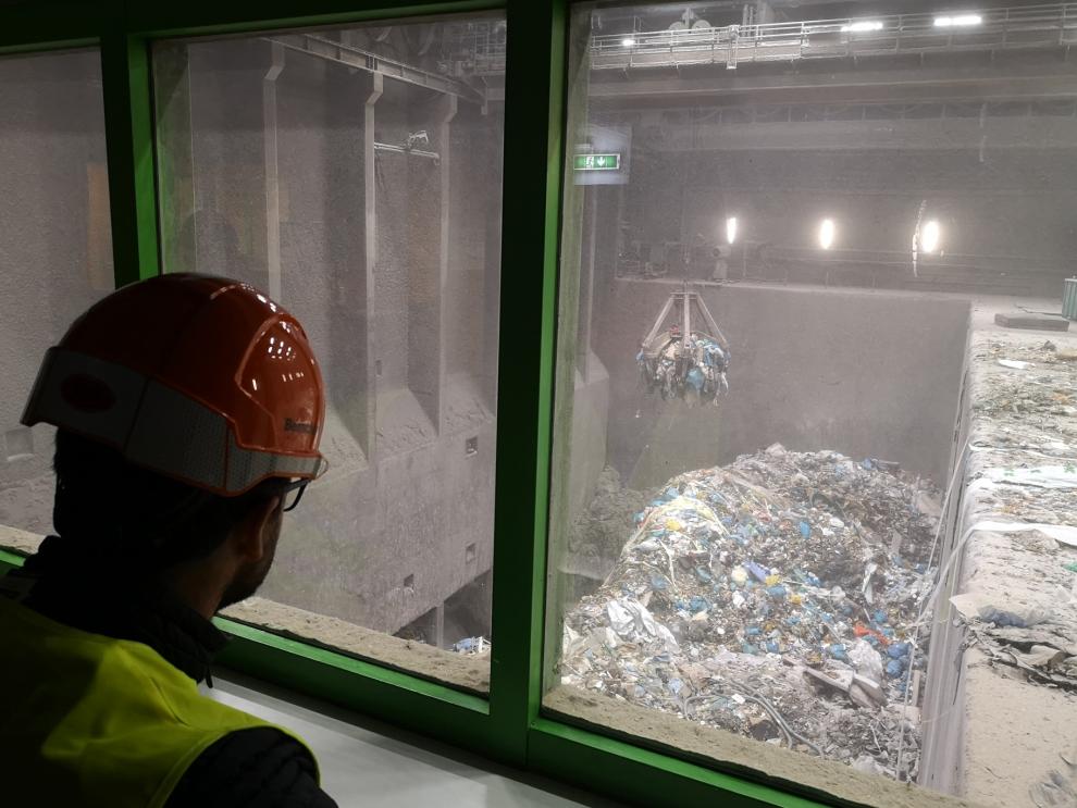 Ein Student, der einen Schutzhelm und eine Warnweste trägt, blickt durch ein Fenster auf einen großen Haufen Abfallmaterial in einem Abfallbunker.