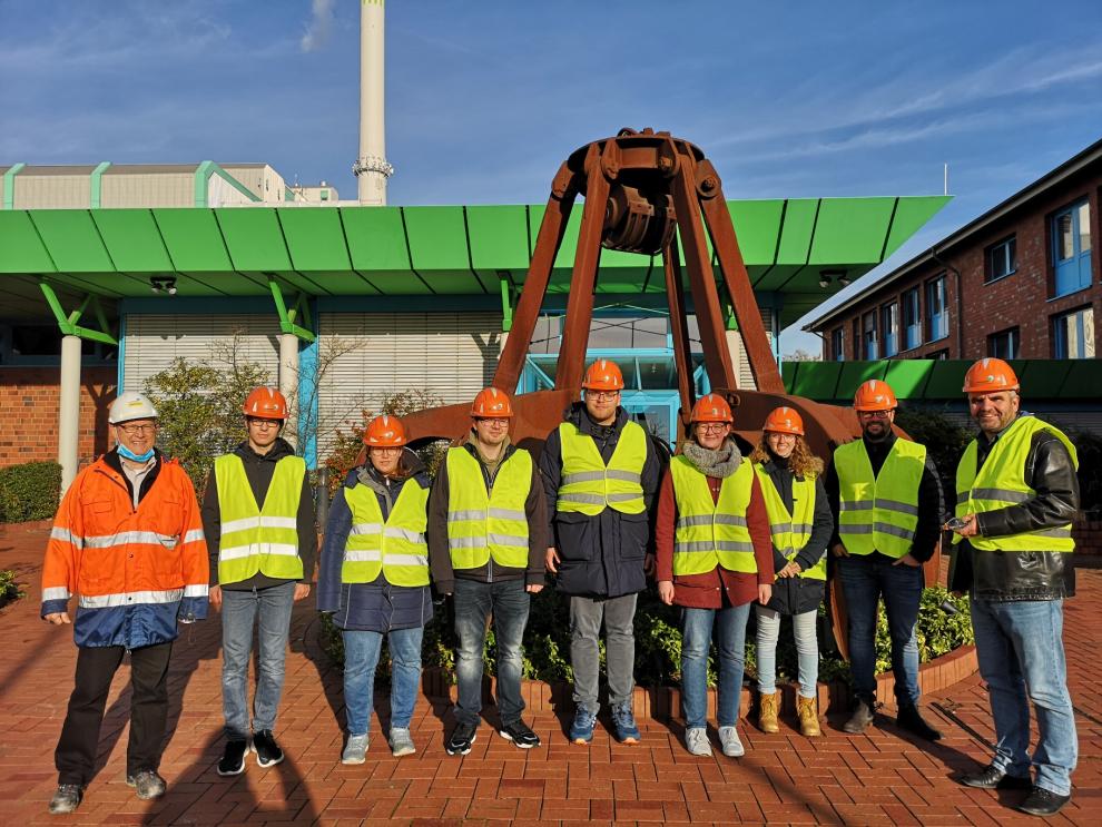 Ein Gruppenfoto vor dem Verwaltungsgebäude des AEZ. Die Personen tragen Schutzhelme und Warnwesten.