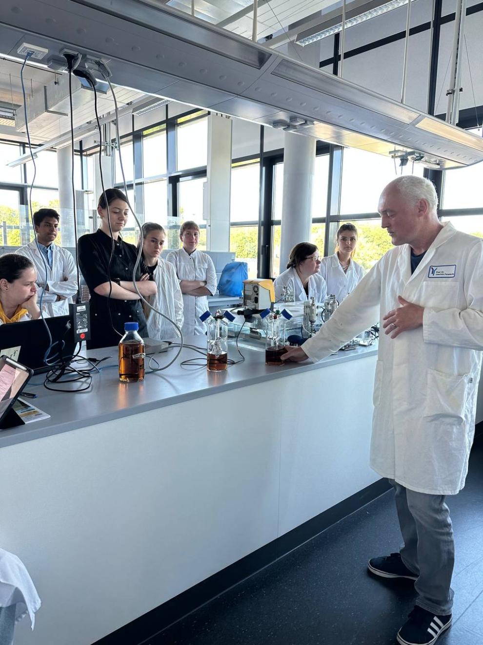 1. A group of students attentively listening to a lecturer explaining in a laboratory setting.