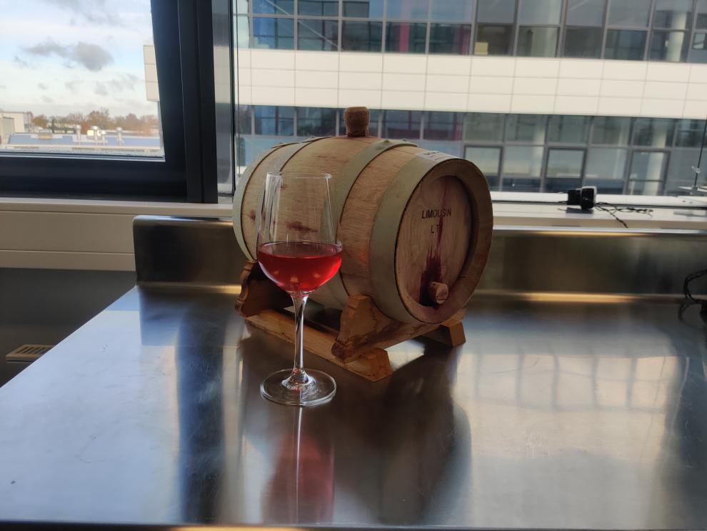 Ein Glas mit roséfarbenem Wein neben einem kleinen Eichenfass. Es vermittelt das Endresultat des Projekts – einen fertigen Wein, bereit für die Verkostung.