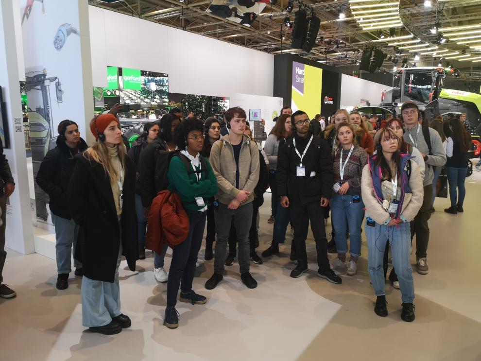 Dieses Foto zeigt eine Gruppe von Studierenden, die aufmerksam eine Präsentation oder Demonstration auf der Agritechnica verfolgen. Sie befinden sich in einer der belebten Hallen, umgeben von landwirtschaftlichen Maschinen und dem Trubel der Veranstaltung. 