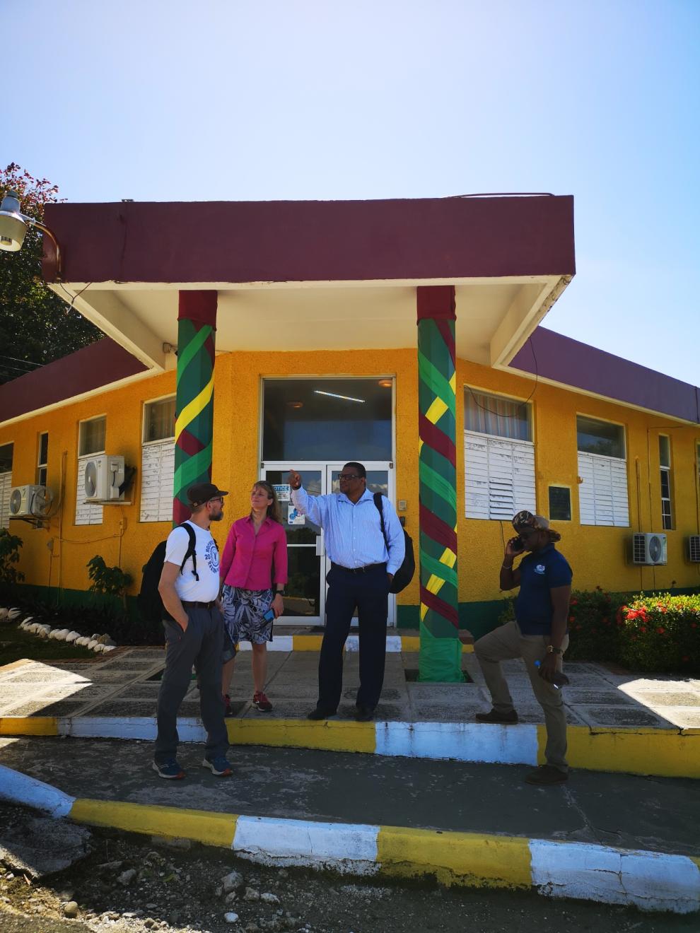 Drei Personen stehen vor einem farbenfrohen Gebäude mit dekorativen Säulen. Sie sind in eine Diskussion vertieft.