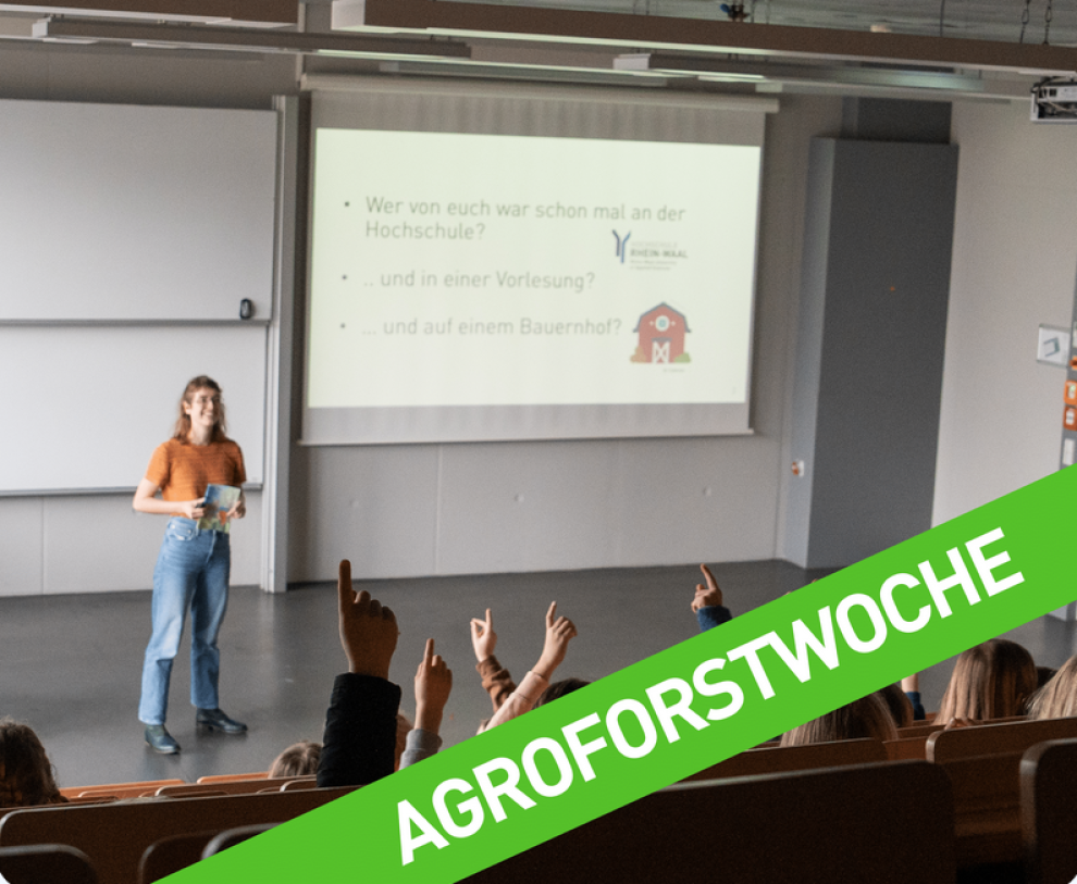 Mehrere Kinder sitzen in einem Hörsaal, während eine Frau vorne eine Präsentation hält.