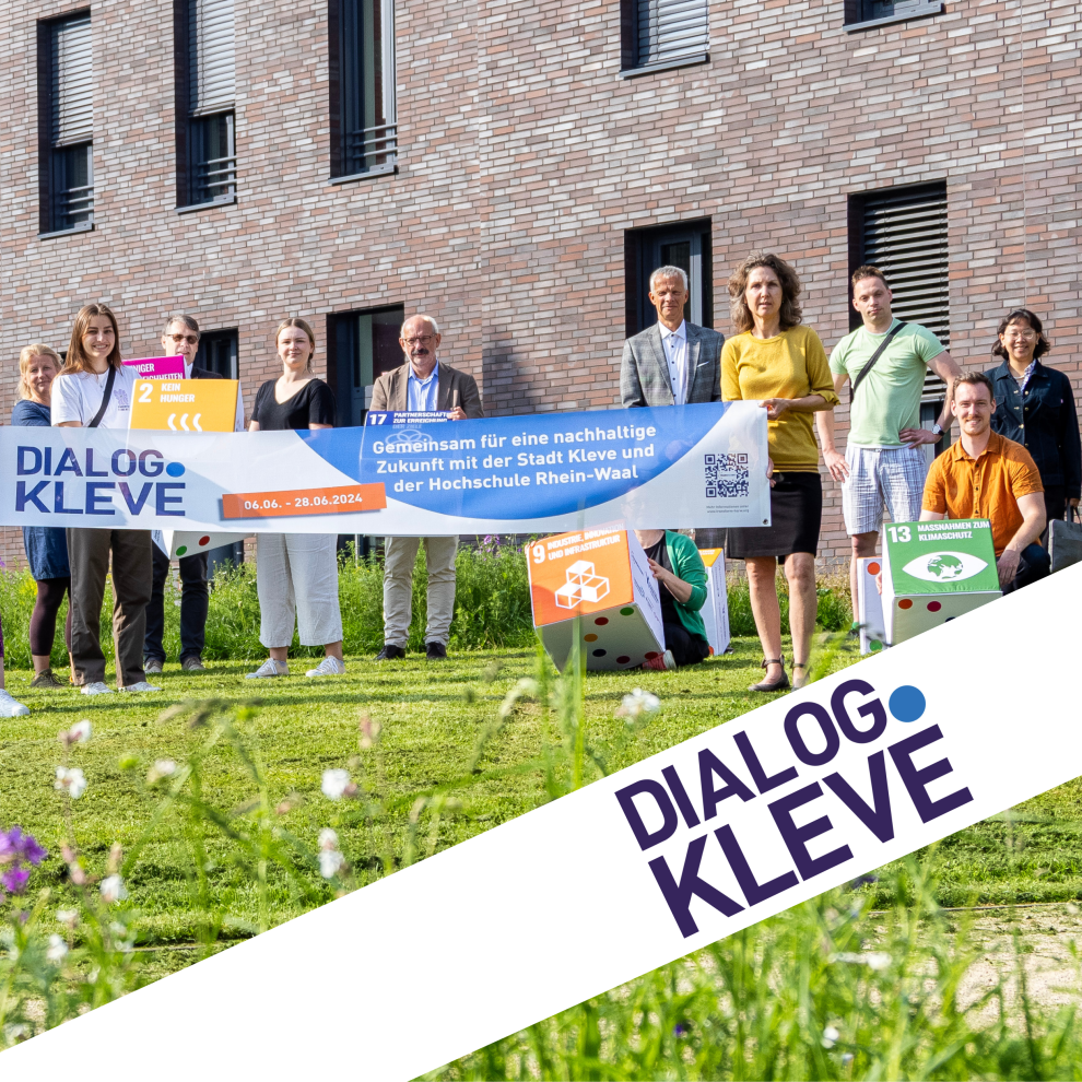 Mehrere Personen stehen auf einer Wiese und halten ein Banner mit dem Titel "Dialog.Kleve" in der Hand.