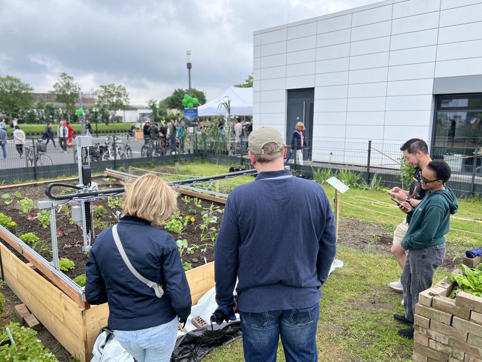 Menschen betrachten den Gartenroboter, der in einem Hochbeet arbeitet. Im Hintergrund sind weitere Besucher und Stände zu sehen.