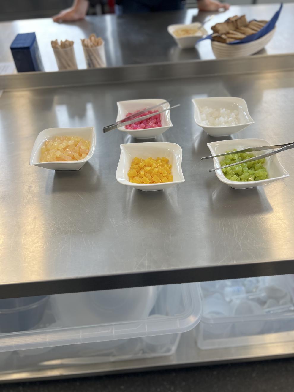 Eine Nahaufnahme von Schalen mit verschiedenen farbigen, würfelförmigen Veganen Gummibären. Diese sind Teil einer Demonstration und Verkostung.