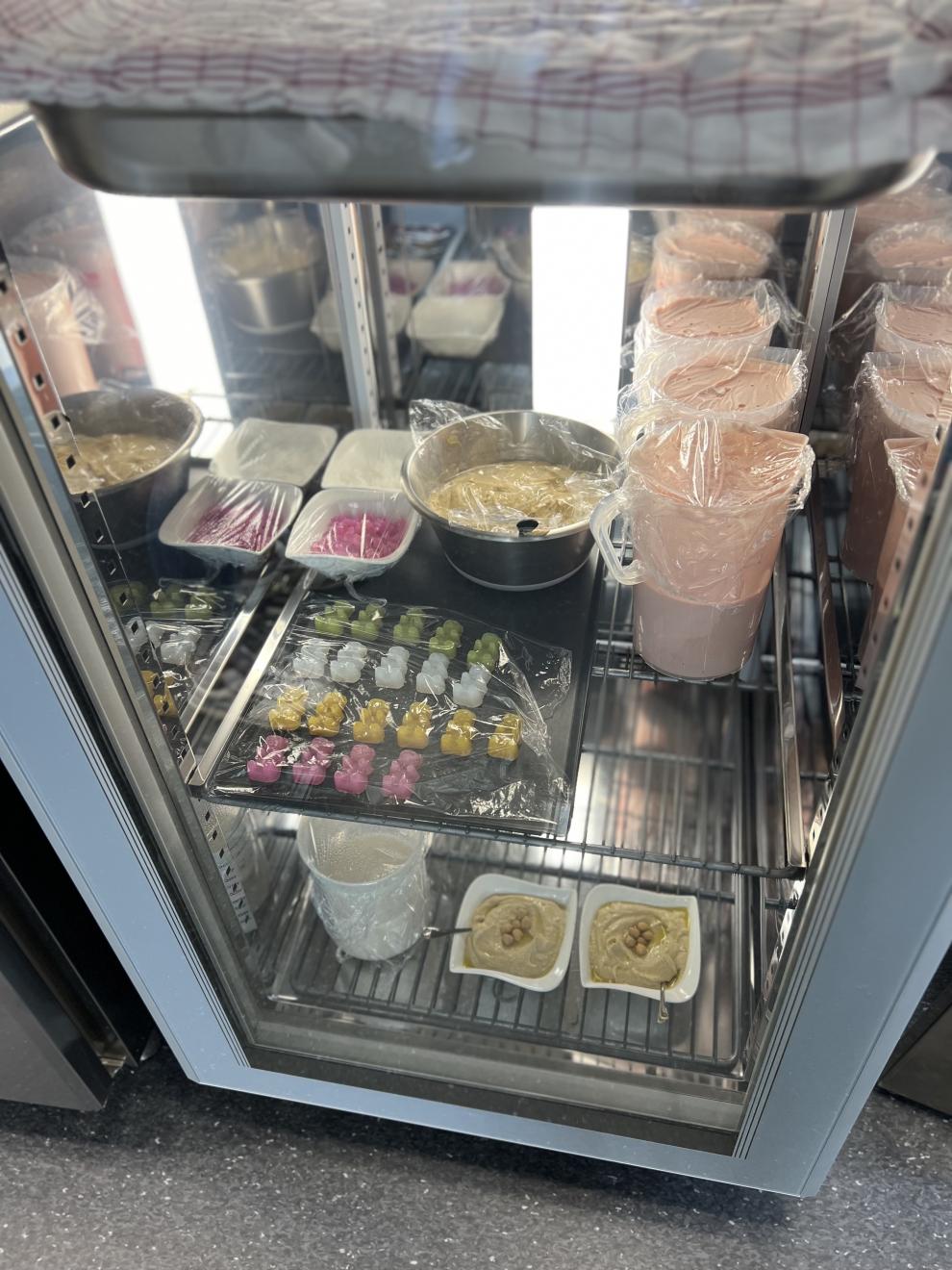 Ein Kühlschrank mit verschiedenen veganen Lebensmitteln und Proben. Einige der Proben sind in Plastik verpackt und in Schüsseln und Behältern gelagert. 