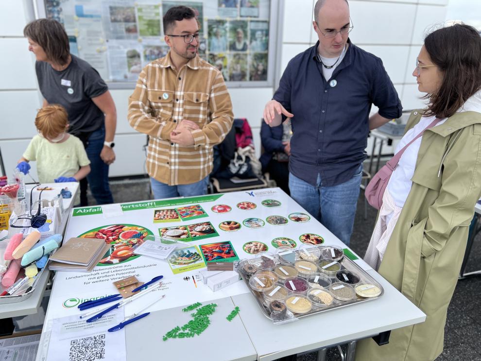 Ein Stand im Freien mit verschiedenen Experimenten und Demonstrationen, die von Erwachsenen und Kindern besucht werden. Die Teilnehmer haben die Möglichkeit, an den Aktivitäten teilzunehmen und mehr über die präsentierten Themen zu lernen.