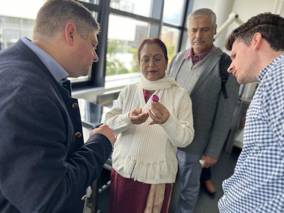 IIT und HSRW Gruppe betrachtet ein kleines Gefäß, das von einer Frau, wahrscheinlich ein Mitglied der Delegation, in der Hand gehalten wird. Es scheint, dass sie etwas untersucht, das ebenfalls im Zusammenhang mit Lebensmittelforschung steht. Der intensive Austausch über wissenschaftliche Inhalte, wie im Dokument beschrieben, ist deutlich sichtbar