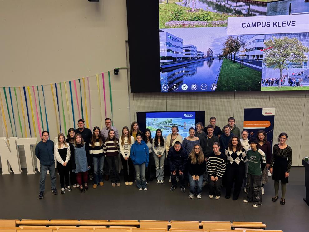 Gruppenfoto der Teilnehmenden und Betreuenden des Herbst-MINT-Festivals  im Foyer der Hochschule Rhein-Waal. Die Gruppe von etwa 25 Schülerinnen und Schülern  steht vor einer großen Leinwand, auf der "CAMPUS KLEVE" zu lesen ist.
