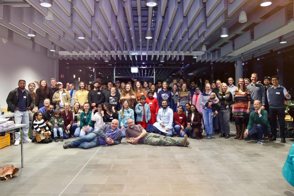 Großes Gruppenfoto aller Teilnehmenden der Jubiläumsfeier, die fröhlich in die Kamera schauen; zwei Personen liegen scherzhaft im Vordergrund auf dem Boden.