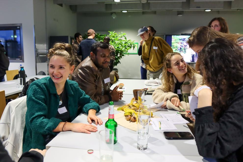 Nahaufnahme einer Tischgruppe, die sich angeregt unterhält und lacht; eine junge Frau im grünen Cardigan lächelt besonders fröhlich, auf dem Tisch liegen Notizzettel und Stifte.