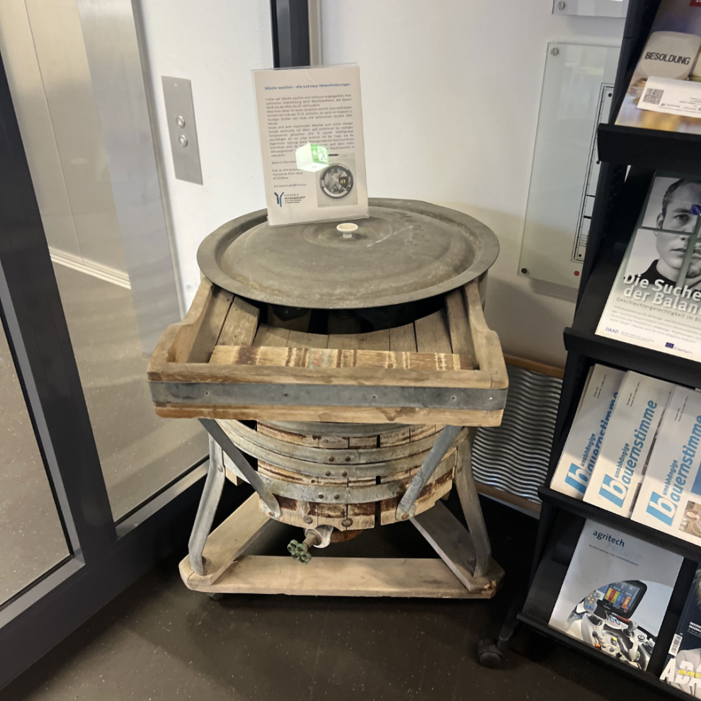 Historische Waschmaschine aus Holz aus der Mitte des 20. Jahrhunderts, bestehend aus einem hölzernen Bottich auf einem Gestell mit Metalldeckel.