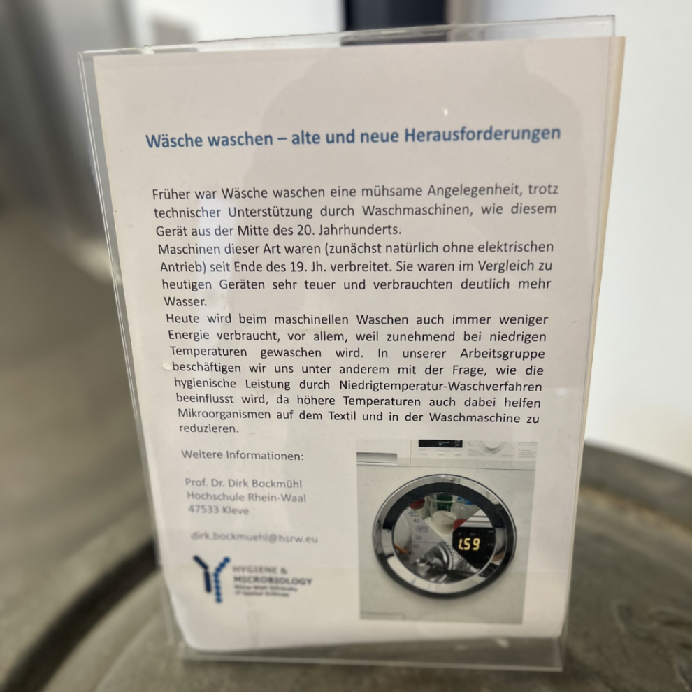 Infotafel auf einer historischen Waschmaschine mit Text zur Geschichte des Waschens und zur aktuellen Hygiene-Forschung von Prof. Dr. Dirk Bockmühl.
