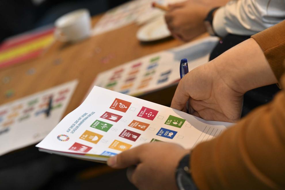 Eine Person hält eine Karte mit Abbildungen der 17 Nachhaltigkeitsziele in den Händen