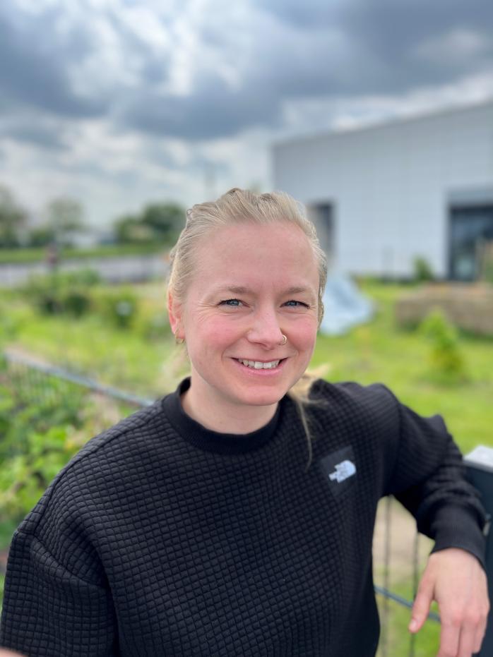 Profilfoto von Natalie Laibach mit schwarzem Pullover vor dem verschwommenen Hintergrund des Gewächshauses